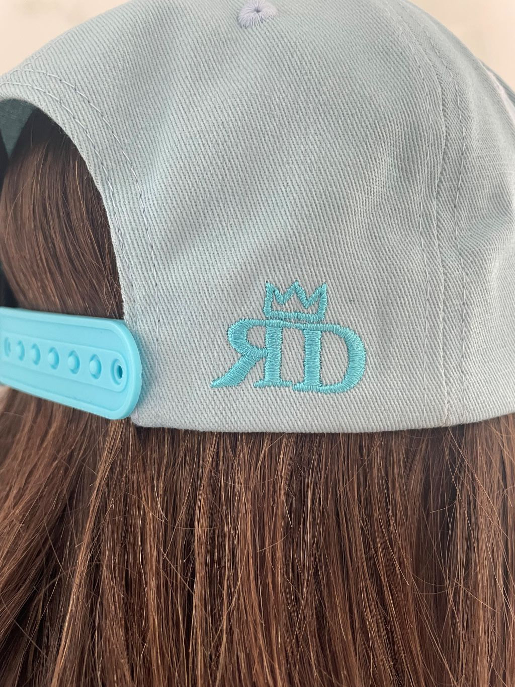 Vue 3/4 arrière droit en plan serré sur le logo REINERT DESIGN  casquette bleu turquoise