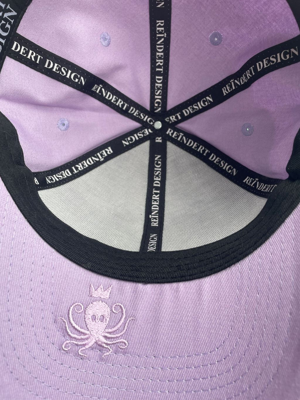 Vue de dessous de la casquette parme clair avec logo pieuvre, poulpe sur le dessous de la visière